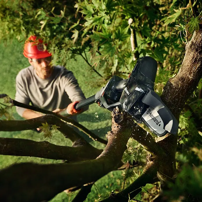 Husqvarna Akku-Kettensäge Aspire P5-P4A - 18 V, Li-Ionen, Ohne Akku, Schwertlänge: 12 cm - Schwarz-graue Husqvarna Astsäge schneidet einen Baumast, gehalten von einer Person in Schutzkleidung.