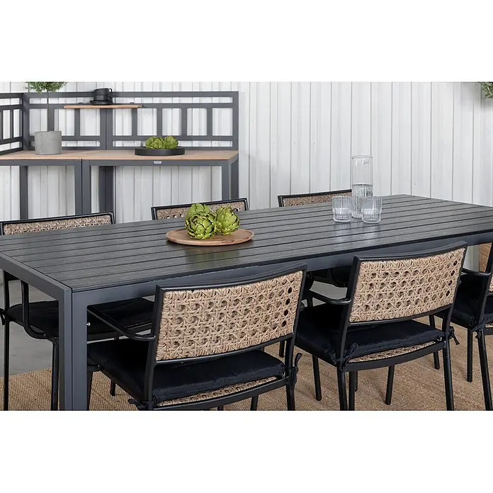 Ebuy24 Gartenstuhl Paola 4er-Set - 100 % Polyester, Rattan, Stahl, Schwarz, B x T x H: 56 x 59 x 78 cm - Garten-Essgruppe: dunkelgrauer Lamellentisch, Stühle mit geflochtenen Rückenlehnen und schwarzen Kissen, auf einem Teppich.