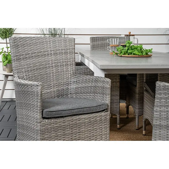 Ebuy24 Gartenstuhl Malin 2er-Set - 100 % Polyester, Aluminium, Rattan, Grau, B x T x H: 58 x 65 x 92 cm - Grauer Kunst-Rattan-Sessel mit dunkelgrauem Kissen, Teil eines Outdoor-Esstischsets auf einer Terrasse.