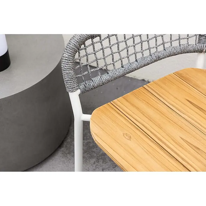 Ebuy24 Gartensessel Amora - 1 Stk., Teak, Grau, B x T x H: 59 x 55 x 88 cm - Nahaufnahme eines modernen Outdoor-Stuhls mit Holzplatte, weißem Gestell und grauem Geflecht, neben einem Betontisch.