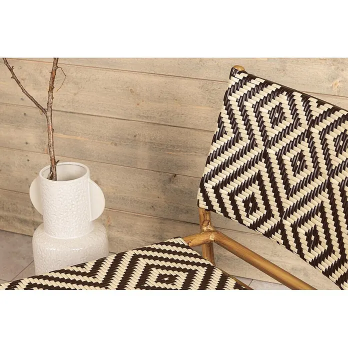 Ebuy24 Gartensessel Calapan - 1 Stk., Aluminum, Rattan, Korbmöbel, Braun, B x T x H: 57 x 69 x 77 cm - Geflochtener Stuhl mit dunkelbraun-beigem geometrischem Muster und Bambusrahmen, neben weißer Vase mit Ast.