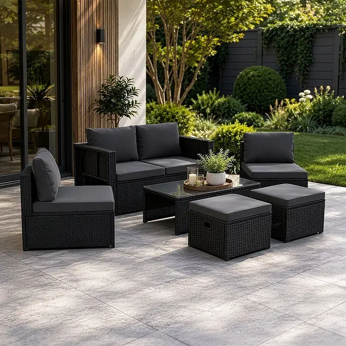 Juskys Loungemöbel-Set Salou - 6 -tlg., Möbel: Polyrattan, Stahl (pulverbeschichtet); Tischplatte: Gehärtetes Glas; Bezug: 100% Polyestergewebe 180 g/m², Farbe Möbel: SchwarzFarbe Polster: GrauMax. Belastbarkeit: Bank 320 kg; Sessel/Hocker je 160 kg; Tisch 75 kg, Schwarz - Schwarzes Rattan-Gartenmöbelset mit grauen Kissen, bestehend aus Sofa, Sessel, Couchtisch und zwei Hockern, auf einer Terrasse.