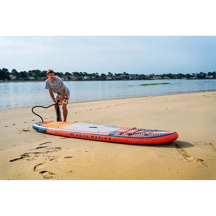 Aqua Marina SUP-Board-Set Atlas - L x B x H: 366 x 86 x 15 cm, Tragkraft: 180 kg, Orange - Eine Person pumpt ein orange-blaues Aqua Marina aufblasbares Stand-Up-Paddleboard am Sandstrand auf.