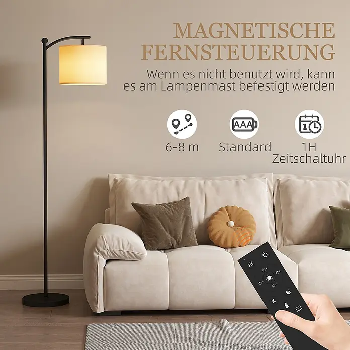 Homcom Stehleuchte - 9 W, Höhe: 159,6 cm, Schwarz, Cremeweiß, E27 - Schwarze Stehlampe mit beigem Schirm im Wohnzimmer. Eine Hand hält die schwarze magnetische Fernbedienung.