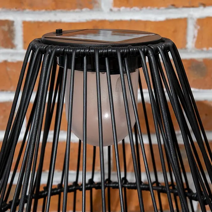 Outsunny Campinglampe - 34 x 34 x 56 cm - Nahaufnahme einer schwarzen Solarlaterne mit mattierter Glühbirne vor einer Ziegelmauer.