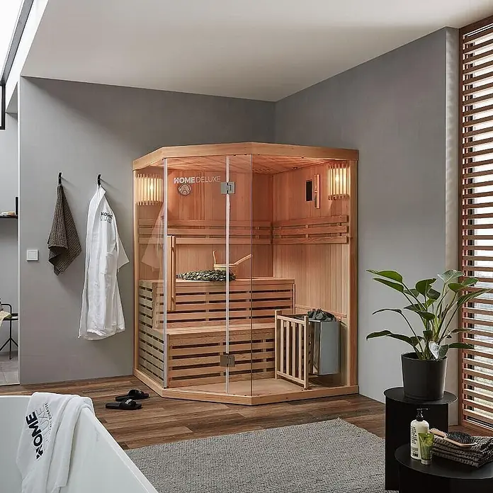 Home Deluxe Elementsauna SKYLINE XL - Elektroofen, Steuerung Ofen: Integriert - Eine Ecksauna aus hellem Holz und Glas mit Bänken und Heizung in einem modernen Badezimmer.