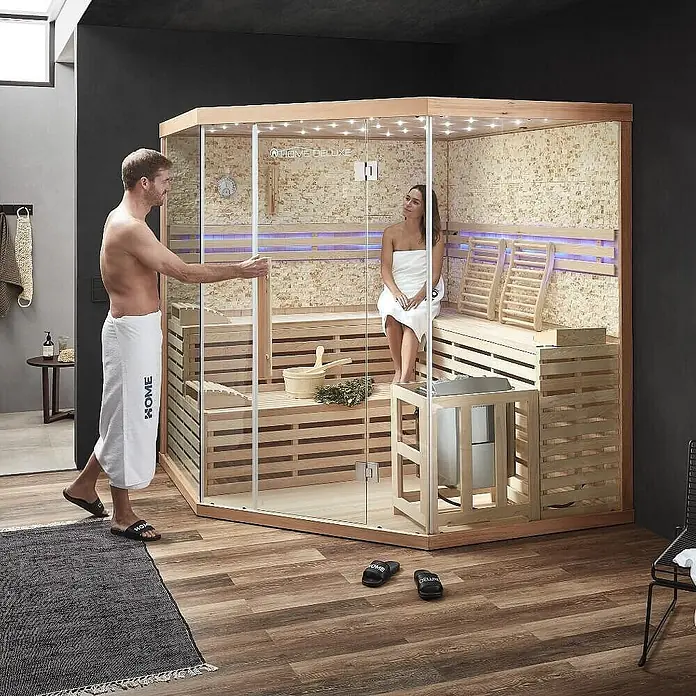 Home Deluxe Elementsauna SKYLINE BIG XL KUNSTSTEINWAND - Elektroofen, Steuerung Ofen: Integriert, L x B x H: 200 x 200 x 210 cm - Moderne Indoor-Sauna mit Glasfront und Holzbänken, von einem Paar genutzt.