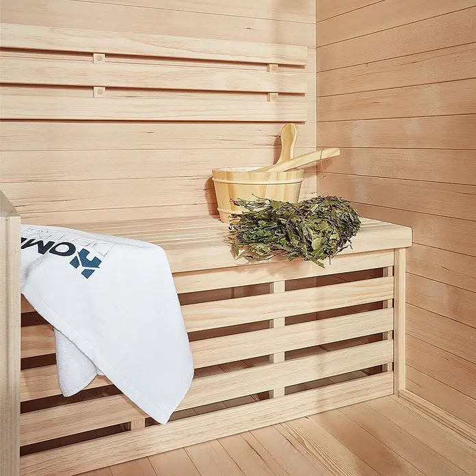 HOME DELUXE - Traditionelle Sauna SKYLINE L - 150 x 120 cm für 3 Personen -  - Hölzerner Saunaeimer, Kelle und getrocknete Blätter auf einer hellen Holzbank, mit einem weißen Handtuch.