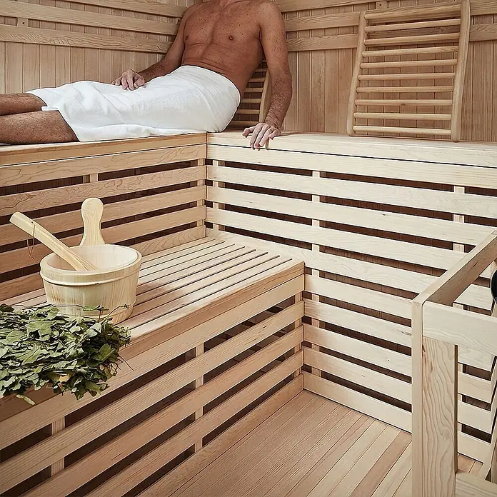 Home Deluxe Elementsauna SKYLINE BIG XL - Elektroofen, Steuerung Ofen: Integriert, L x B x H: 200 x 200 x 210 cm - Mann entspannt in heller Holzsauna mit Holzeimer, Kelle und getrockneten Blättern auf der unteren Bank.