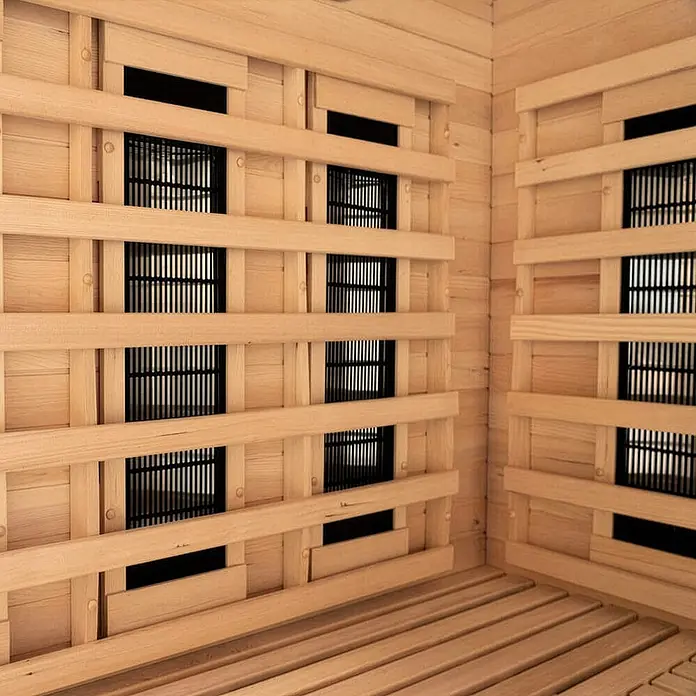 Home Deluxe Infrarotkabine SAHARA L -  - Innenansicht einer hellen Holzsauna mit mehreren schwarzen Gittern für Infrarotheizungen an den Wänden und einem Lattenrostboden.