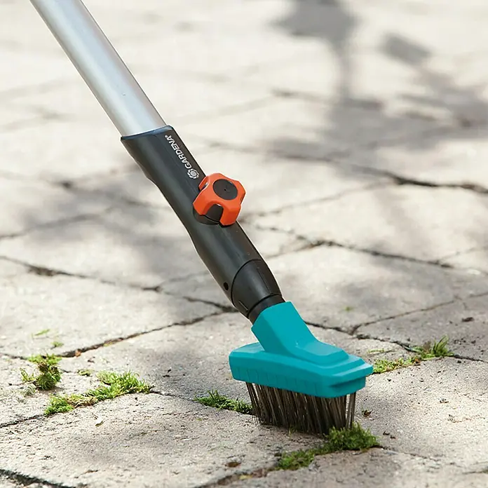Gardena Combisystem Fugenbürste - Mit Stiel - Detailaufnahme einer Gardena Fugenkratzbürste mit Teleskopstiel beim Entfernen von Unkraut aus Pflasterfugen.