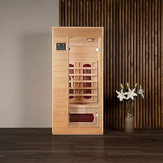 Home Deluxe Infrarotkabine REDSUN S -  - Helle Holz-Saunakabine mit Glastür, Bedienfeld und dunkelroten Innenelementen in einem modernen Raum.