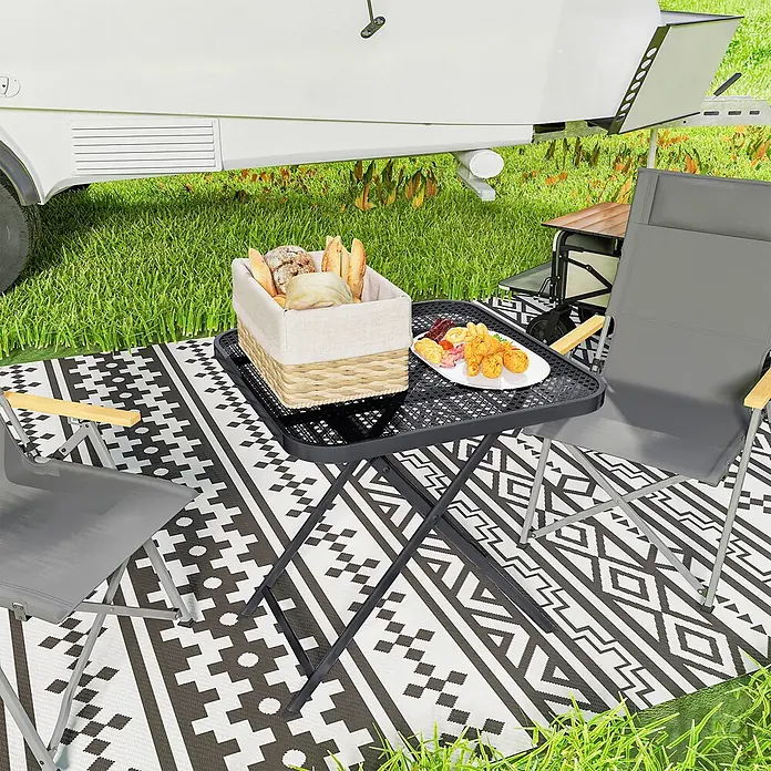 Outsunny Garten-Beistelltisch - Stahl, Klappbar, Quadratisch, Schwarz - Schwarzer faltbarer Metalltisch und zwei graue Campingstühle mit schwarz-weiß gemustertem Outdoor-Teppich, zum Camping genutzt.