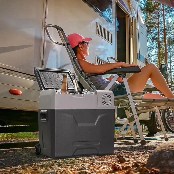 Homcom Garten-Aufbewahrungsbox - L x B x H: 58,6 x 37,8 x 54,5 cm - Ein grauer und schwarzer tragbarer Kühler mit Rädern, gefüllt mit Eis und Flaschen, von einer Person neben einem Wohnmobil verwendet.