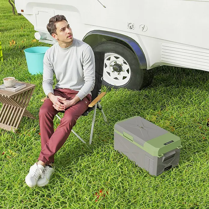 Outsunny Garten-Aufbewahrungsbox - L x B x H: 60,2 x 32 x 27 cm - Eine grau-grüne Kühlbox steht auf dem Gras neben einem Wohnwagen für Outdoor-Kühlung.