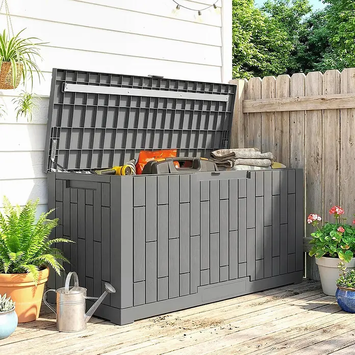 Outsunny Garten-Aufbewahrungsbox - L x B x H: 122,5 x 56 x 62 cm - Große dunkelgraue Outdoor-Aufbewahrungsbox mit Holzoptik, Deckel offen, mit Gartengeräten und Decken auf einer Holzterrasse.