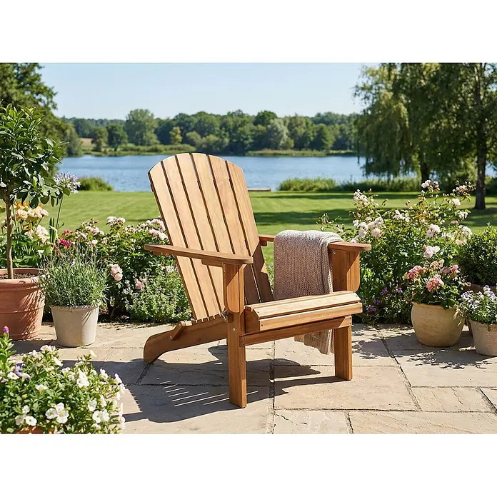 Prestige Home Living Outdoor Gartenstuhl Adirondack -  - Ein hölzerner Adirondack-Stuhl mit einer hellen Decke auf der Armlehne steht auf einer Terrasse am See, umgeben von Topfpflanzen.