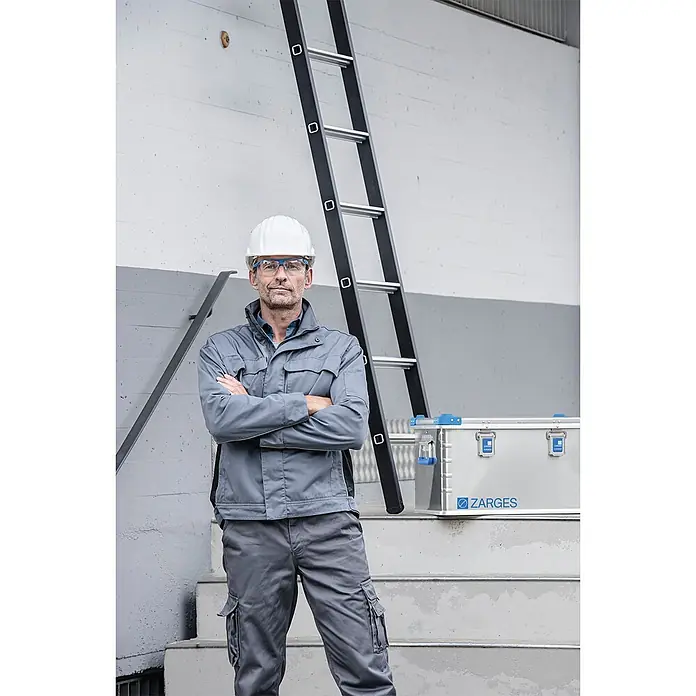 Zarges Aufbewahrungsbox Eurobox Volumen 60l Innenmaß 550x350x310mm -  - Ein Mann in Arbeitskleidung steht neben einer schwarzen Leiter und einer silbernen ZARGES-Aluminiumbox auf Betontreppen.