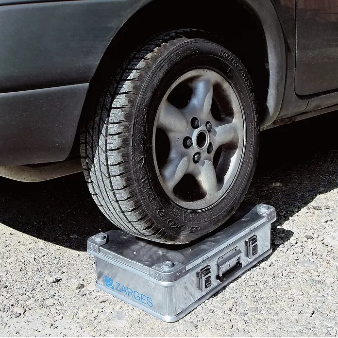 Zarges Aufbewahrungsbox Universalkiste K470 IP 65 Aluminium 239 l - Aluminium - Silberne Zarges Aluminiumbox mit einem Autoreifen darauf, die ihre extreme Robustheit demonstriert.