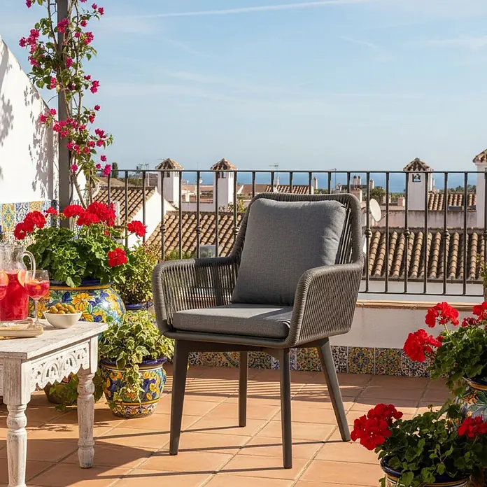 Bene Living Gartenstuhl-Set Marbella - 2 Stk., Aluminium mir Rope-Geflecht, grau - Grauer Outdoor-Sessel mit Kissen auf einer sonnigen Terrakotta-Terrasse, mit Blick auf Dächer und Meer.