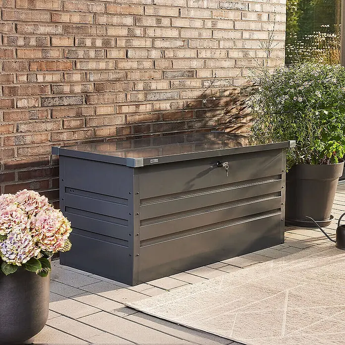 Home Deluxe Garten-Aufbewahrungsbox MEGABOX XXL Größe: 600L - L x B x H: 158 x 64 x 62 cm, Anthrazitgrau, Stahl - Dunkelgraue Metall-Outdoor-Aufbewahrungsbox auf einer Terrasse, mit Schlüssel im Schloss.