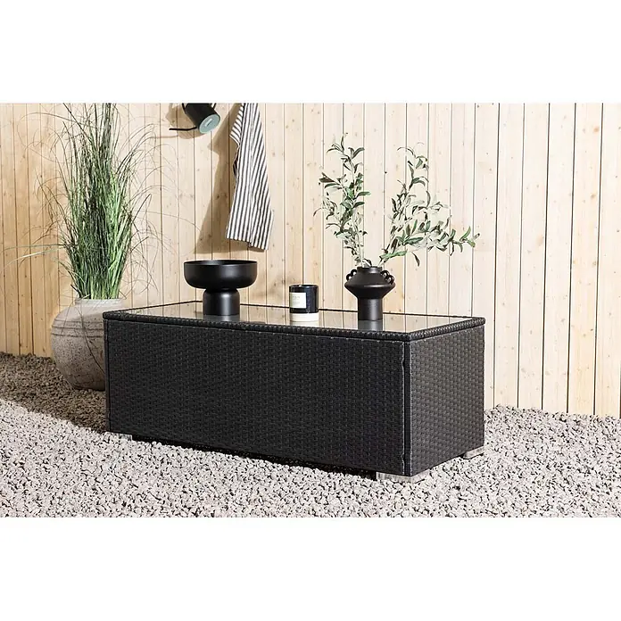 Ebuy24 Garten-Loungetisch London - L x B x H: 50 x 120 x 45 cm, Ø x H: 50 x 45 cm, Korbmöbel, Schwarz, Stapelbar - Schwarzer Outdoor-Couchtisch aus geflochtenem Material mit Glasplatte, auf Kies in einer Gartenumgebung.
