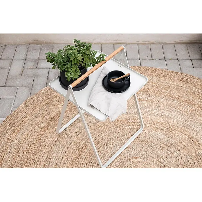 Ebuy24 Garten-Beistelltisch Clarin - L x B x H: 45 x 45 x 59 cm, Stahl, Teak, Stapelbar, Sonstige, Beige - Weißer klappbarer Beistelltisch mit Holzgriff, der draußen auf einem Jute-Teppich eine Pflanze und eine schwarze Tasse trägt.