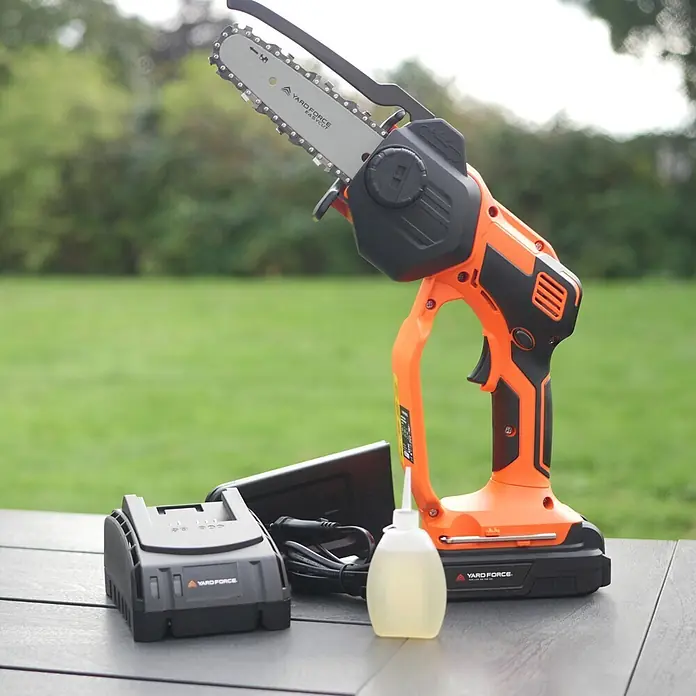 Yard Force Einhand-Akku-Kettensäge LS C13 - 2 Ah, 1 Akku - Yard Force orange-schwarze Akku-Mini-Kettensäge mit Ladegerät und Ölflasche auf einem Tisch.