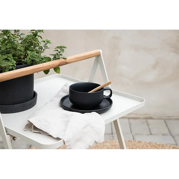 Ebuy24 Garten-Beistelltisch Clarin - L x B x H: 45 x 45 x 59 cm, Stahl, Teak, Stapelbar, Sonstige, Beige - Schwarzes Keramik-Tassen- und Untertassen-Set mit Holzlöffel und Leinentuch auf einem weißen Tabletttisch.