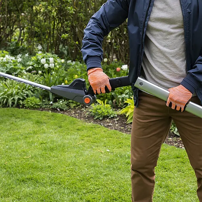 Yard Force Akku-Heckenschere iFlex LH F35 - 1 Akku, Schnittlänge: 35 cm - Eine Person im Garten bedient eine graue und silberne Stielheckenschere mit orangefarbenen Handschuhen.