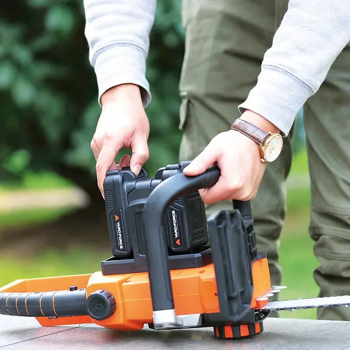 Yard Force Einhand-Akku-Kettensäge LS C35 - 20 V, 2 Ah, 2 Akkus, Schwertlänge: 35 cm - Hände einer Person beim Anpassen von Akkus an einer orange-schwarzen Akku-Kettensäge.