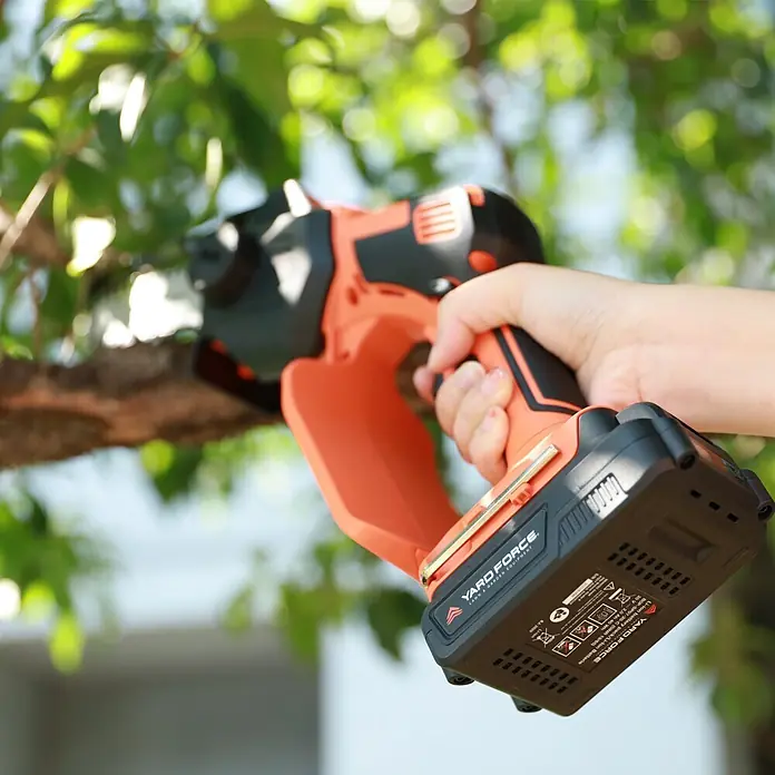 Yard Force Einhand-Akku-Kettensäge LS C13 - 2 Ah, 1 Akku - Orange-schwarze Akku-Astschere in einer Hand, schneidet einen Ast.