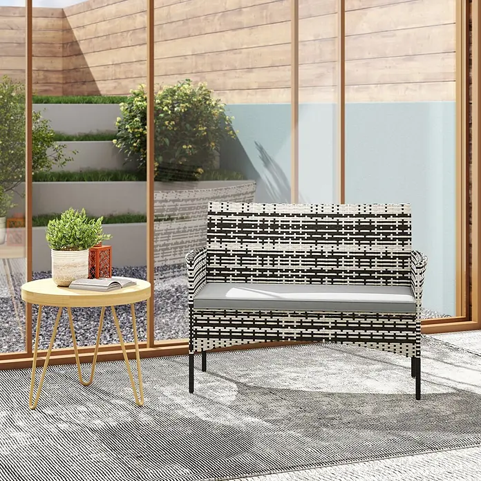 Outsunny Loungesofa - B x T x H: 63 x 63 x 85 cm, PE-Rattan, Hellgrau - Schwarz-weiß geflochtene Outdoor-Bank mit grauem Kissen, auf einer Terrasse neben einem kleinen Tisch.