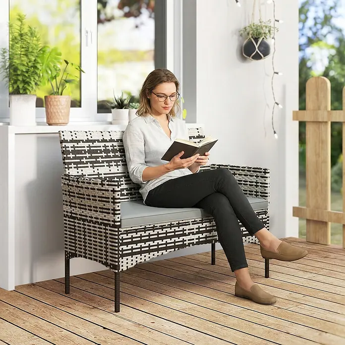 Outsunny Loungesofa - B x T x H: 63 x 63 x 85 cm, PE-Rattan, Hellgrau - Zweisitzer-Outdoor-Bank aus schwarzem und weißem Geflecht mit grauem Kissen, wird von einer lesenden Frau genutzt.