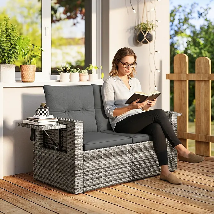 Outsunny Loungesofa - B x T x H: 63 x 63 x 68 cm, Stahl, PE-Rattan, Hellgrau, Dunkelgrau, Schwarz - Graues Rattan Zweiersofa für den Außenbereich mit dunklen Polstern und ausklappbarem Beistelltisch, von Person auf Terrasse genutzt.