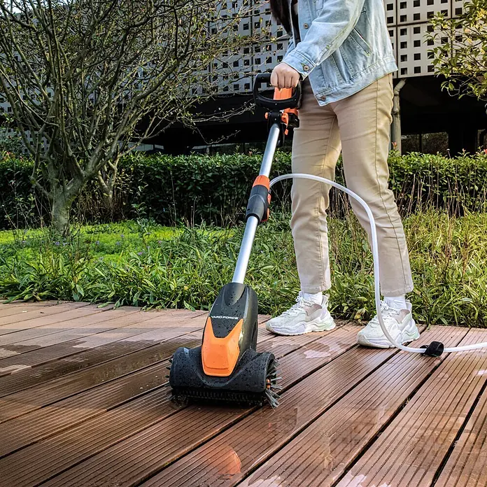 Yard Force Akku-Reinigungsbürste LW CPC1 - 20 V, 1 Akku, 4 Ah - Eine Person reinigt eine nasse Holzterrasse mit einem schwarz-orangen YARD FORCE Schrubber, verbunden mit einem weißen Schlauch.