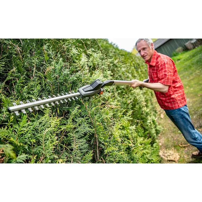Yard Force Akku-Heckenschere iFlex LH F35 - 1 Akku, Schnittlänge: 35 cm - Mann schneidet eine grüne Hecke mit einer Langstiel-Heckenschere mit silbernen Klingen und dunkelgrauem Gehäuse.