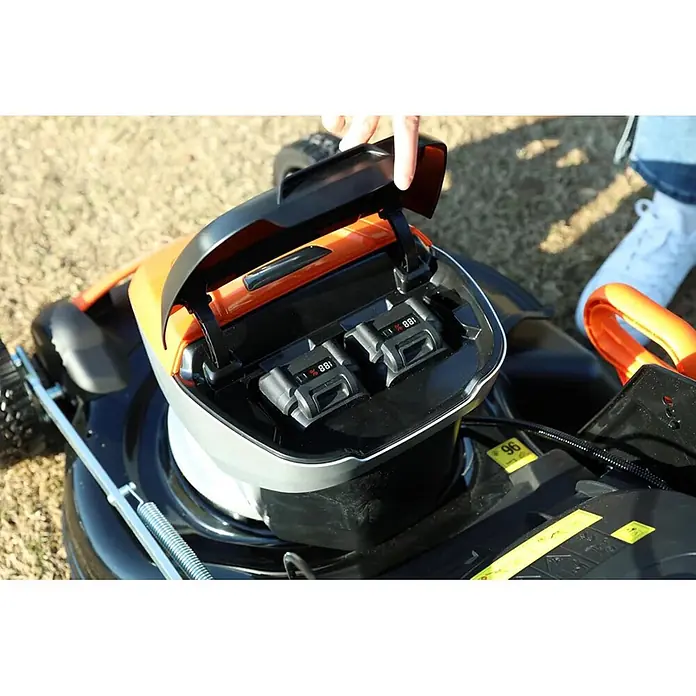 Yard Force Akku-Rasenmäher LM C46 - 40 V, 1 Akku, 5 Ah, Schnittbreite: 46 cm - Eine Hand öffnet den Deckel eines schwarz-orangen Akku-Rasenmähers, der zwei Batterien mit Ladeanzeige zeigt.