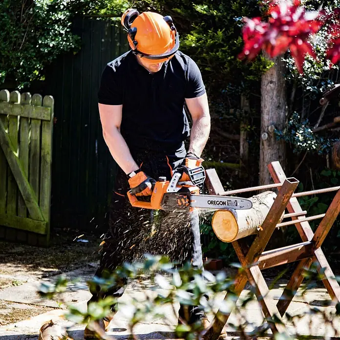 Yard Force Einhand-Akku-Kettensäge LS C35 - 20 V, 2 Ah, 2 Akkus, Schwertlänge: 35 cm - Orange-schwarze Oregon Kettensäge schneidet Holzstamm auf Sägebock, bedient von Person mit Schutzausrüstung.
