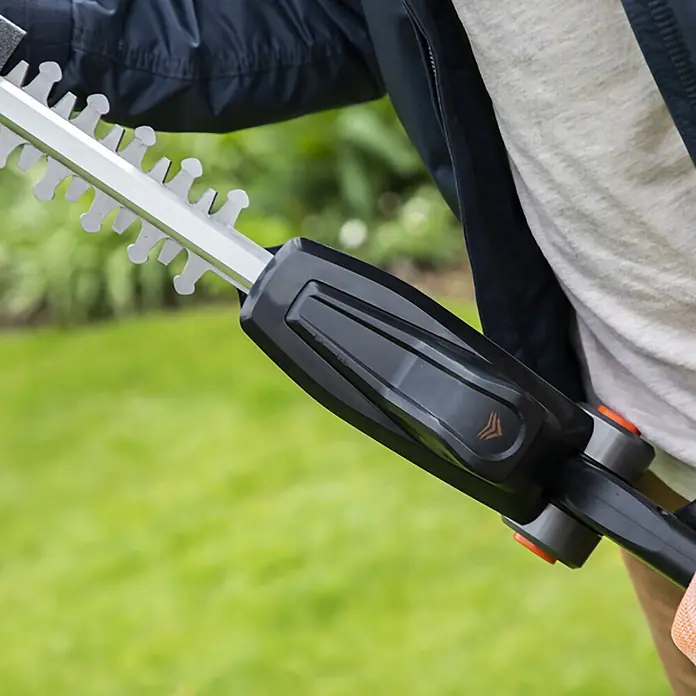 Yard Force Akku-Heckenschere iFlex LH F35 - 1 Akku, Schnittlänge: 35 cm - Person bedient eine Heckenschere mit silberner Klinge und schwarzem Griff mit orangen Details.