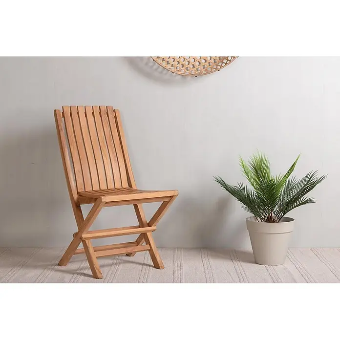 Ebuy24 Gartenstuhl Ghana - Teak, Natur, B x T x H: 48 x 47 x 93 cm - Klappbarer Stuhl aus Naturholz neben einer künstlichen Palme im Topf.