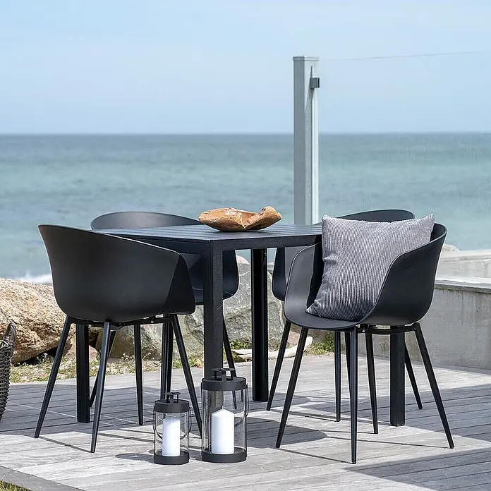Ebuy24 Gartenstuhl Rolino 2er-Set - 2 Stk., Kunststoff Sitz und Stahlbeine, Schwarz, B x T x H: 57 x 70 x 80 cm - Schwarzes Outdoor-Esszimmer-Set mit Stühlen und Tisch auf einer Holzterrasse am Meer.