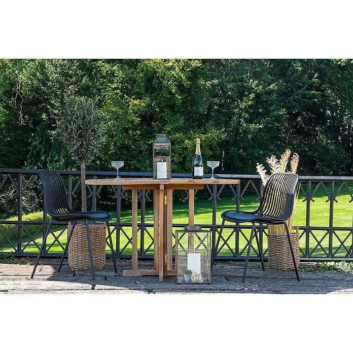 Ebuy24 Gartenstuhl Branson 4er-Set - 4 Stk., PP, Stahl, Schwarz, B x T x H: 47 x 55 x 82 cm - Eine Outdoor-Bistro-Gruppe mit Holztisch, zwei schwarzen Stühlen und Laternen, bereit für Champagner auf einer Terrasse.