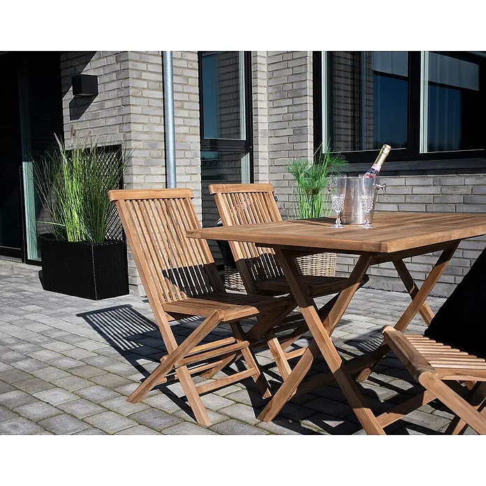 Ebuy24 Gartenstuhl Torad - Teakholz massiv, Braun, B x T x H: 62 x 46 x 89 cm - Ein Teakholz-Gartenmöbelset mit quadratischem Falttisch und Klappstühlen auf einer Terrasse mit Getränken.