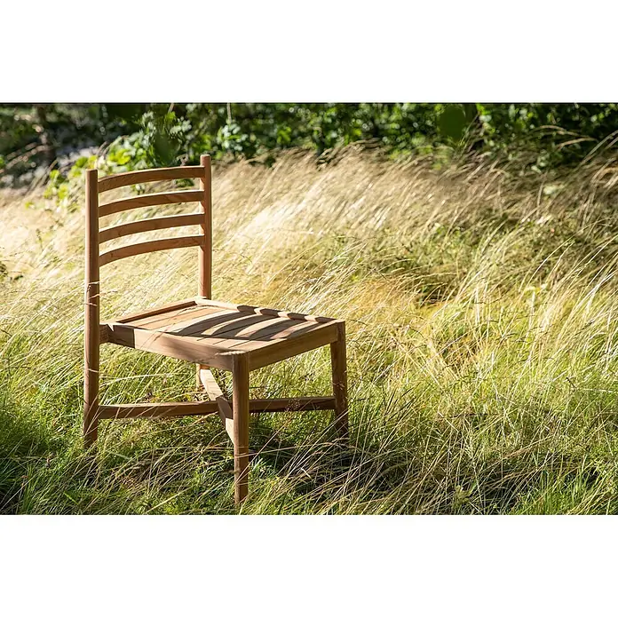 Ebuy24 Gartenstuhl Kenya - 1 Stk., Teak, Teak Dekor, B x T x H: 50 x 52 x 80 cm - Heller Holzstuhl mit Lattenrücken und -sitz, steht im hohen Gras im Freien.