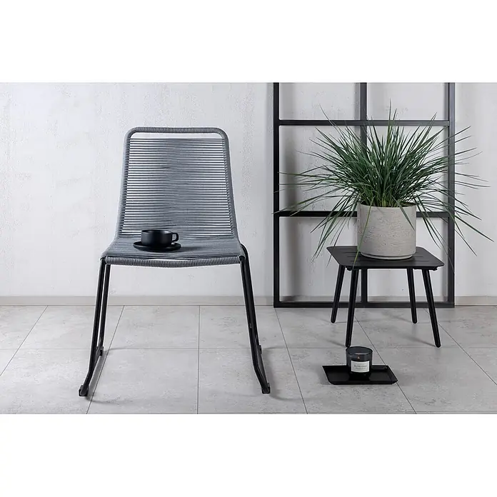 Ebuy24 Gartenstuhl Lindos 4er-Set - 4 Stk., 100 % Polyester (Seil), Stahl, Grau - Grauer Seilstuhl mit schwarzen Beinen, auf dem eine schwarze Tasse steht, neben einem schwarzen Beistelltisch mit Pflanze.
