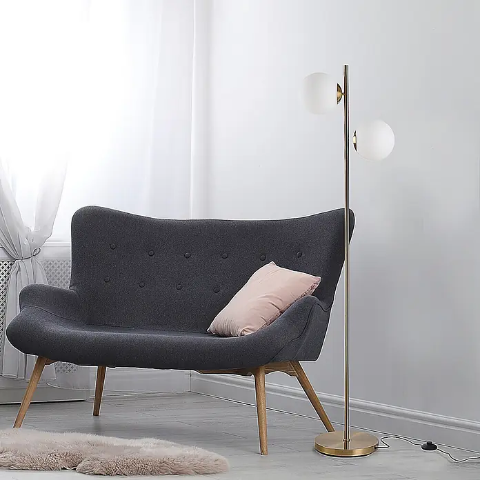 Homcom Stehleuchte - 40 W, Höhe: 165 cm, Gold, Weiß, E27 - Goldene Stehleuchte mit zwei kugelförmigen weißen Glasschirmen, neben einem dunkelgrauen Sofa in einem hellen Raum.