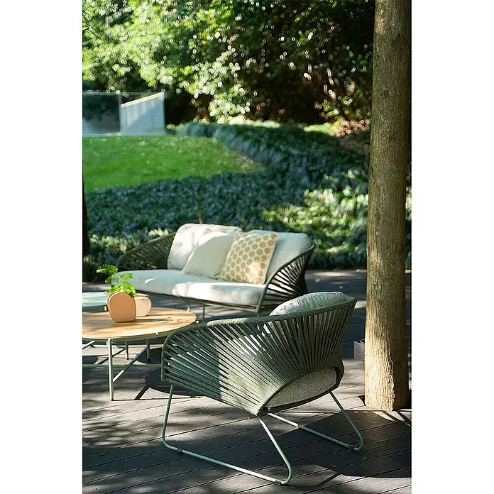 Ebuy24 Loungemöbel-Set Novella - 5 -tlg., Schaum, Polyester, Stahl, Grau - Grünes geflochtenes Outdoor-Sofa und Sessel mit hellen Kissen auf einer Terrasse mit Holztisch im Garten.
