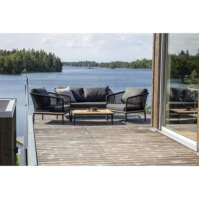 Ebuy24 Loungemöbel-Set Andorra - 4 -tlg., Polyester Seil Stahl, Schwarz - Schwarzes Outdoor-Lounge-Set aus Geflecht mit dunkelgrauen Kissen und Holztisch auf einer Terrasse am See.