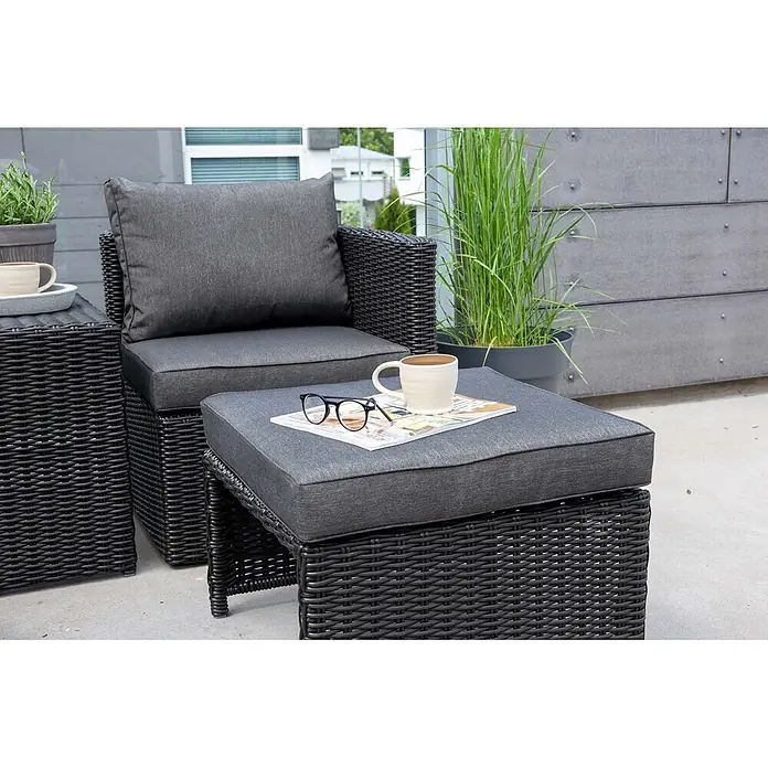 Ebuy24 Loungemöbel-Set Quad - 5 -tlg., Korbmöbel, Schwarz - Dunkelgrauer Rattan-Sessel für den Außenbereich mit passendem Hocker und Kissen. Eine Tasse, Brille und Zeitschrift liegen auf dem Hocker.